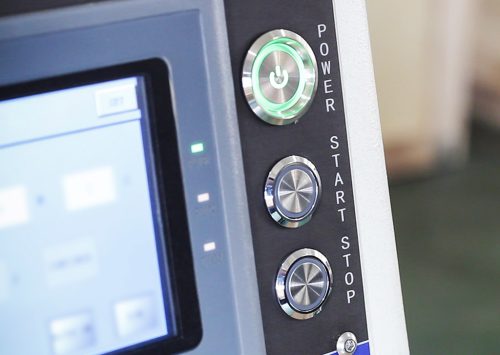Close-up of a touchscreen control panel with power, start, and stop buttons on machinery.