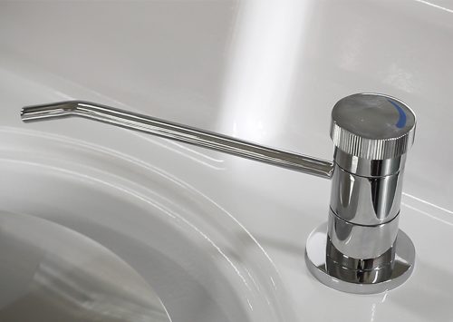 Chrome soap dispenser with long spout on a white bathroom sink, offering a modern and sleek design.