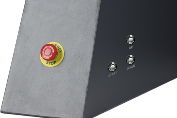 Control panel with red emergency stop button and silver start, up, down buttons on a gray and black machine surface.