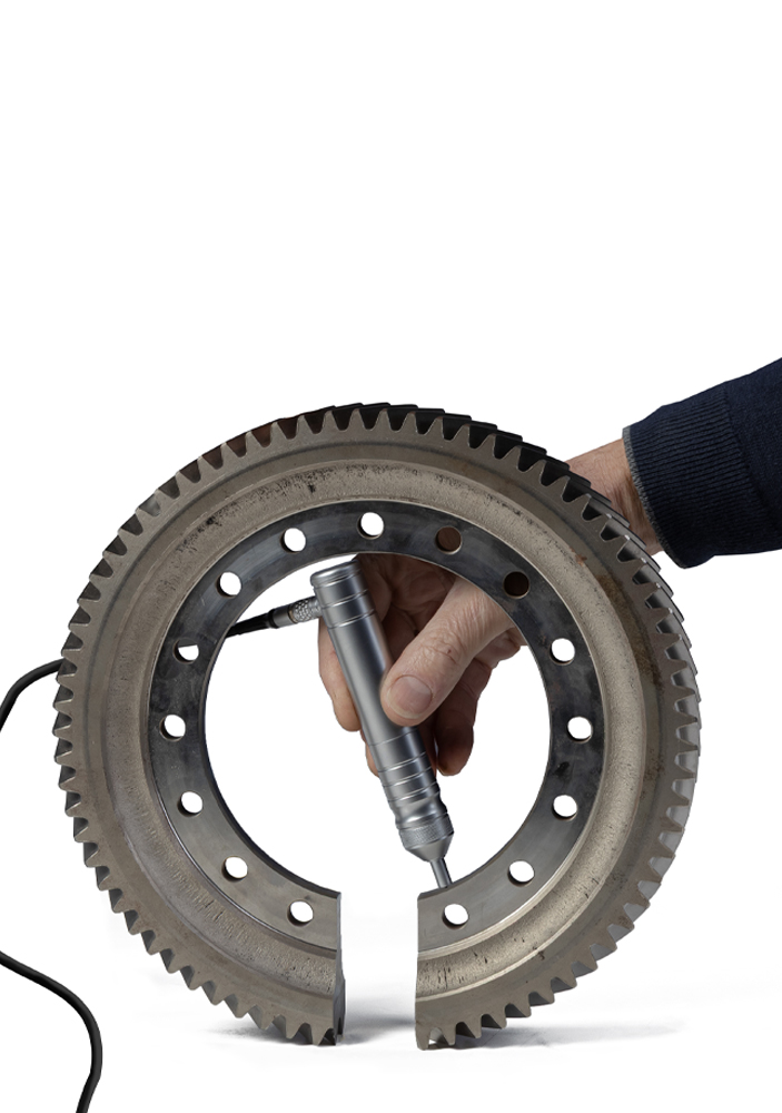 Hand using a tool to measure a large metal gear with precision, showcasing technology and engineering.