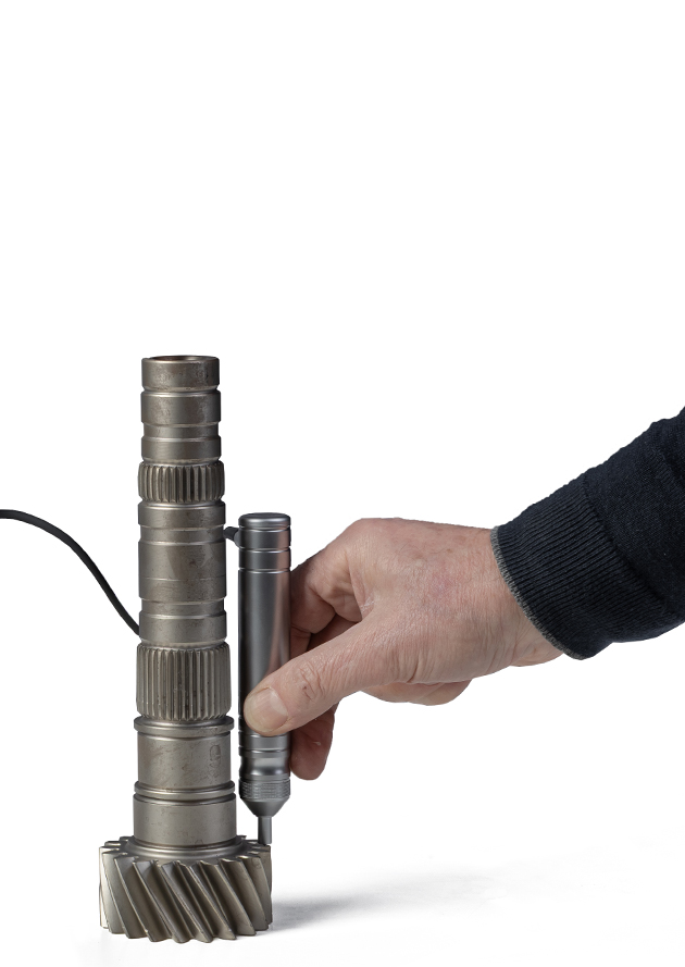 Hand inspecting metal gear shaft with precision tool on white background.
