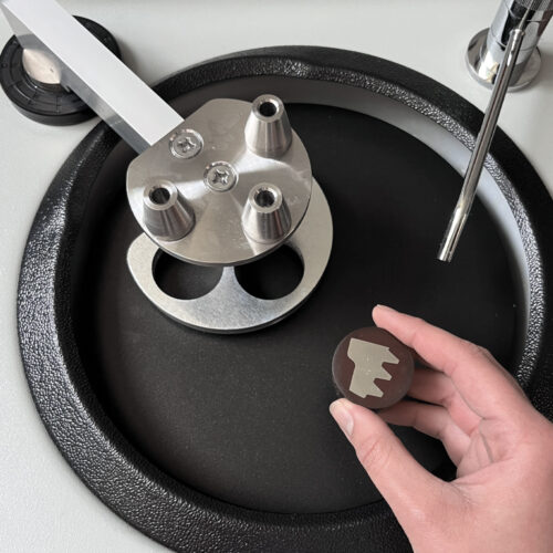 Hand holding a metal part near a polishing machine, showcasing industrial equipment and tools.