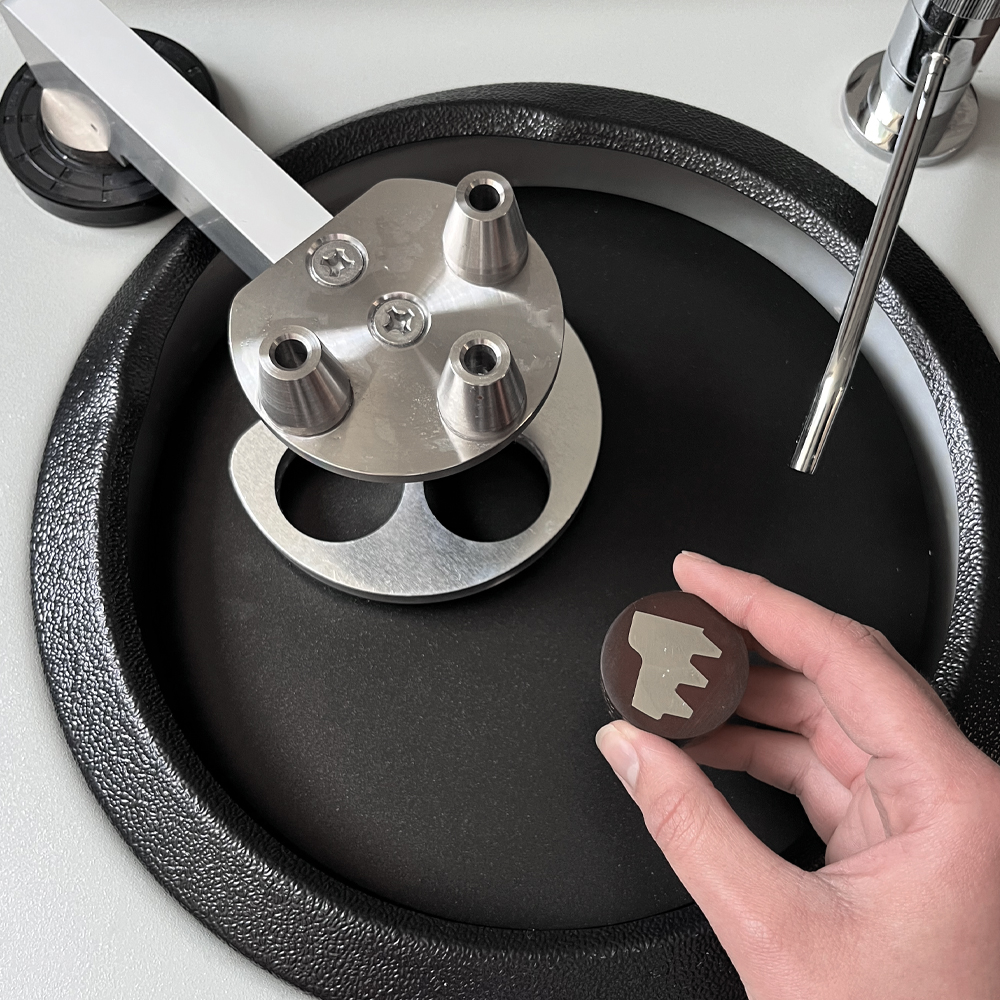 Hand holding a metal part near a polishing machine, showcasing industrial equipment and tools.