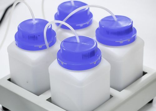 Four laboratory bottles with blue caps and tubes in a holder, used for scientific experiments.